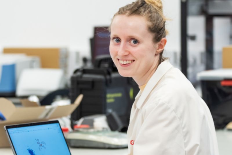 Female wearing a white lab coat sitting with on a laptop